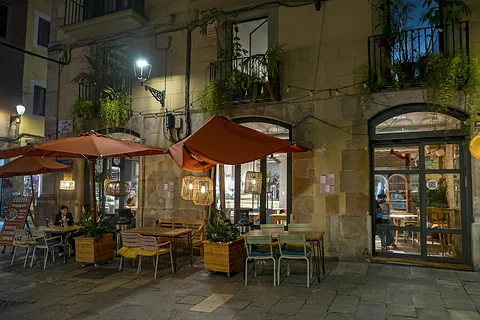 Terras met oranje parasols en tafeltjes in een oude straat in Barcelona, 's avonds verlicht