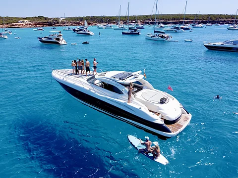 Motorjacht in helder turquoise water voor de kust van Ibiza, met zeilboten op de achtergrond